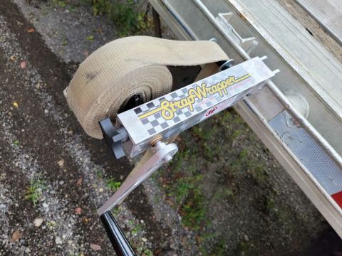 StrapWrapper clamped to a flatbed trailer rail with a tan nylon cargo strap wound on the spool
