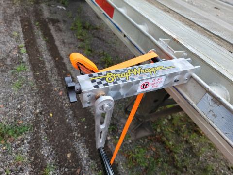 StrapWrapper mounted on the side of an aluminum flatbed cargo bed with the crank handle down