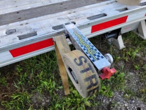 Neatly wound tan cargo strap resting on the StrapWrapper beside a trailer