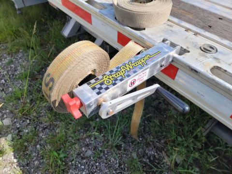 StrapWrapper on a semi trailer rail with an orange strap wound and ready to store